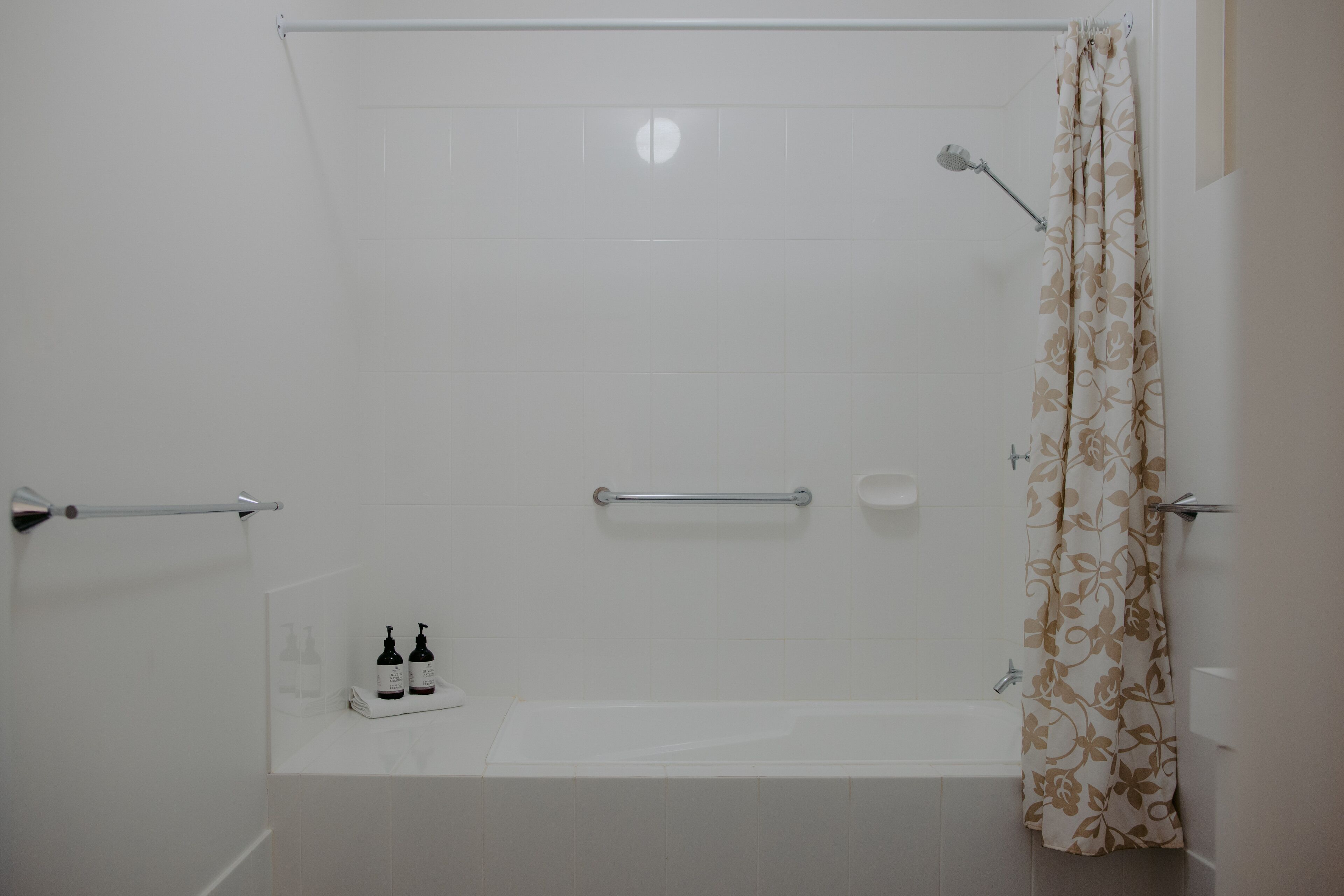 Baño con bañera, ducha e inodoro. Se observan barras de apoyo y un perchero para toallas.