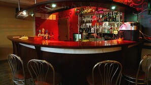 Una zona de bar con una barra curva, sillas metálicas y una variedad de botellas y vasos.