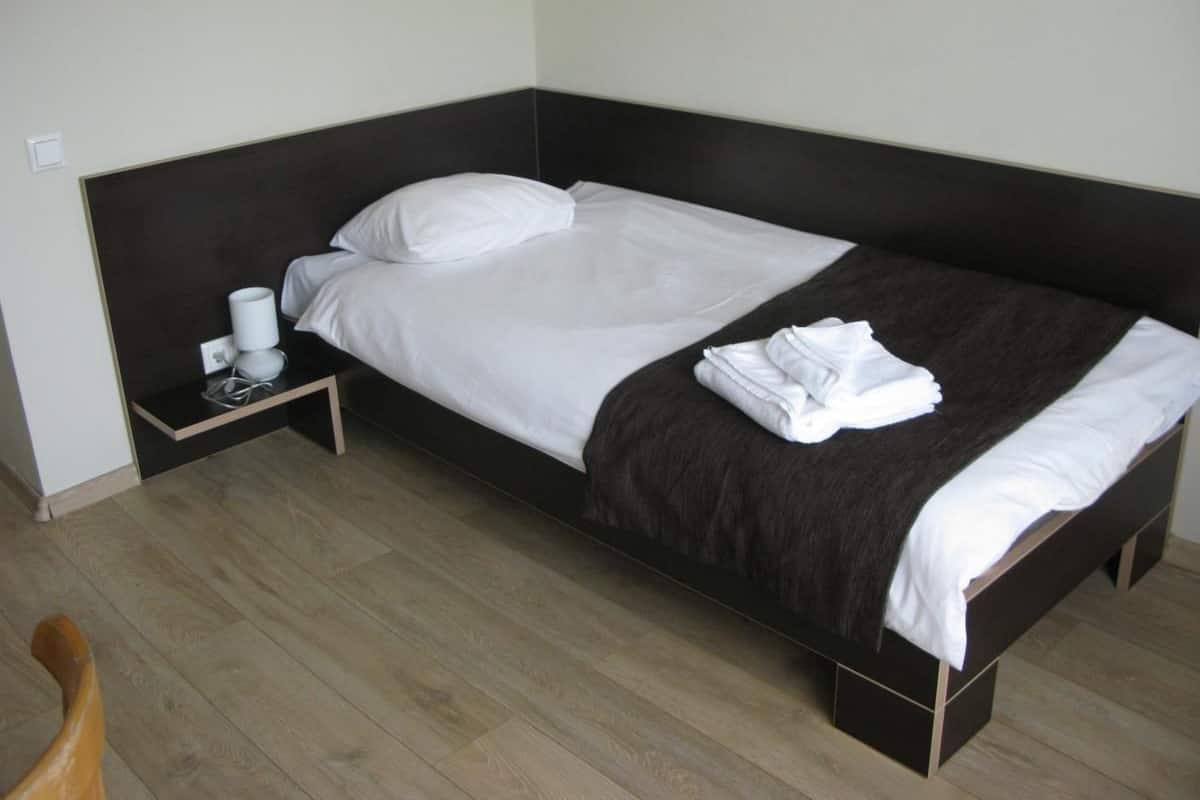 Un lit simple avec une tête de lit sombre, une literie blanche et une petite table de chevet sur laquelle se trouvent une tasse et une boîte de mouchoirs.