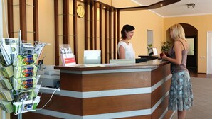 Un mostrador de recepción con detalles de madera, un reloj en la pared y un revistero a la izquierda.