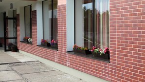 Un edificio con fachada de ladrillo rojo, ventanas amplias con macetas de flores y una puerta a la vista.