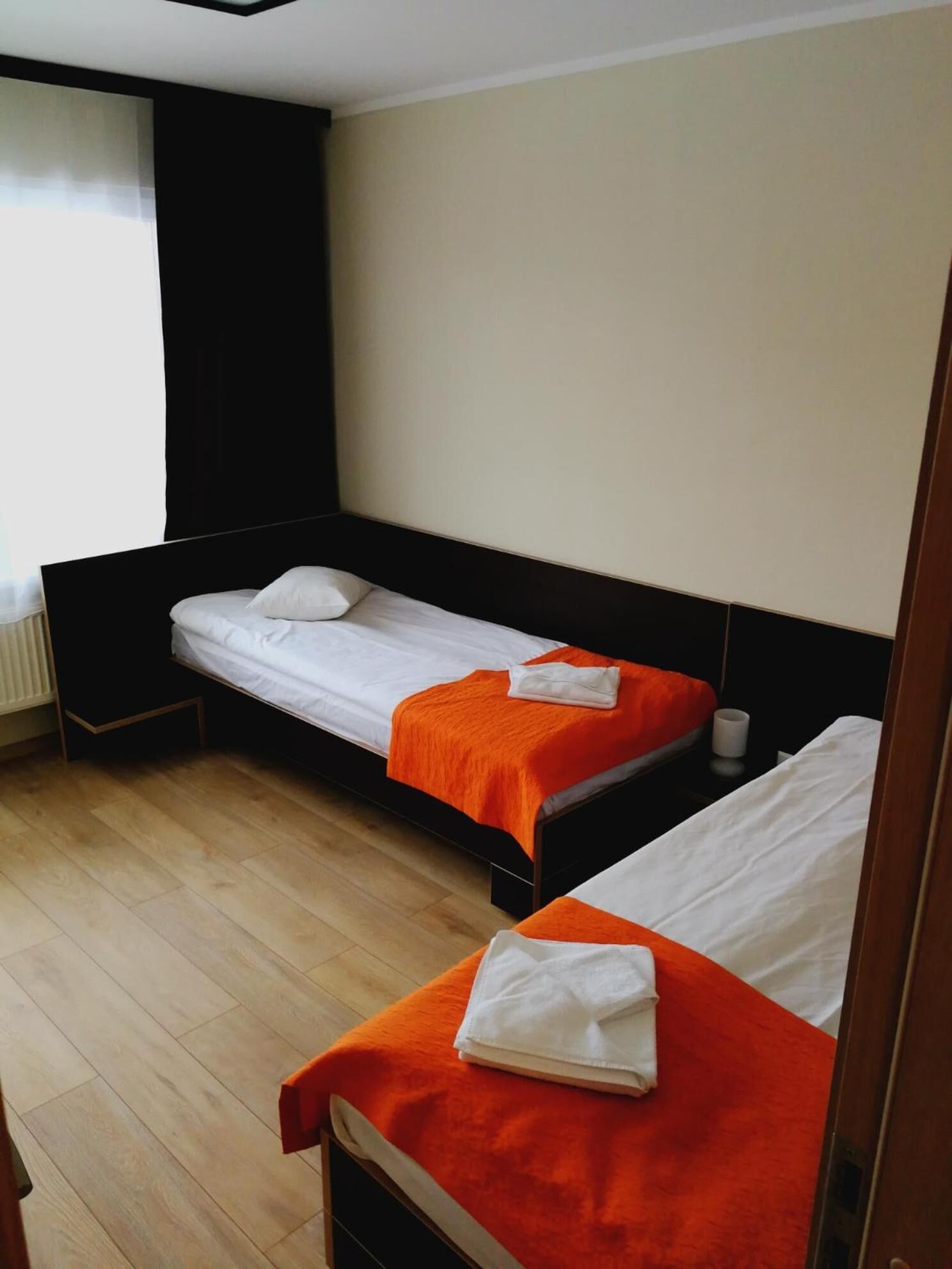 Una camera d'albergo con due letti singoli, ciascuno con coperta arancione e cuscini bianchi.