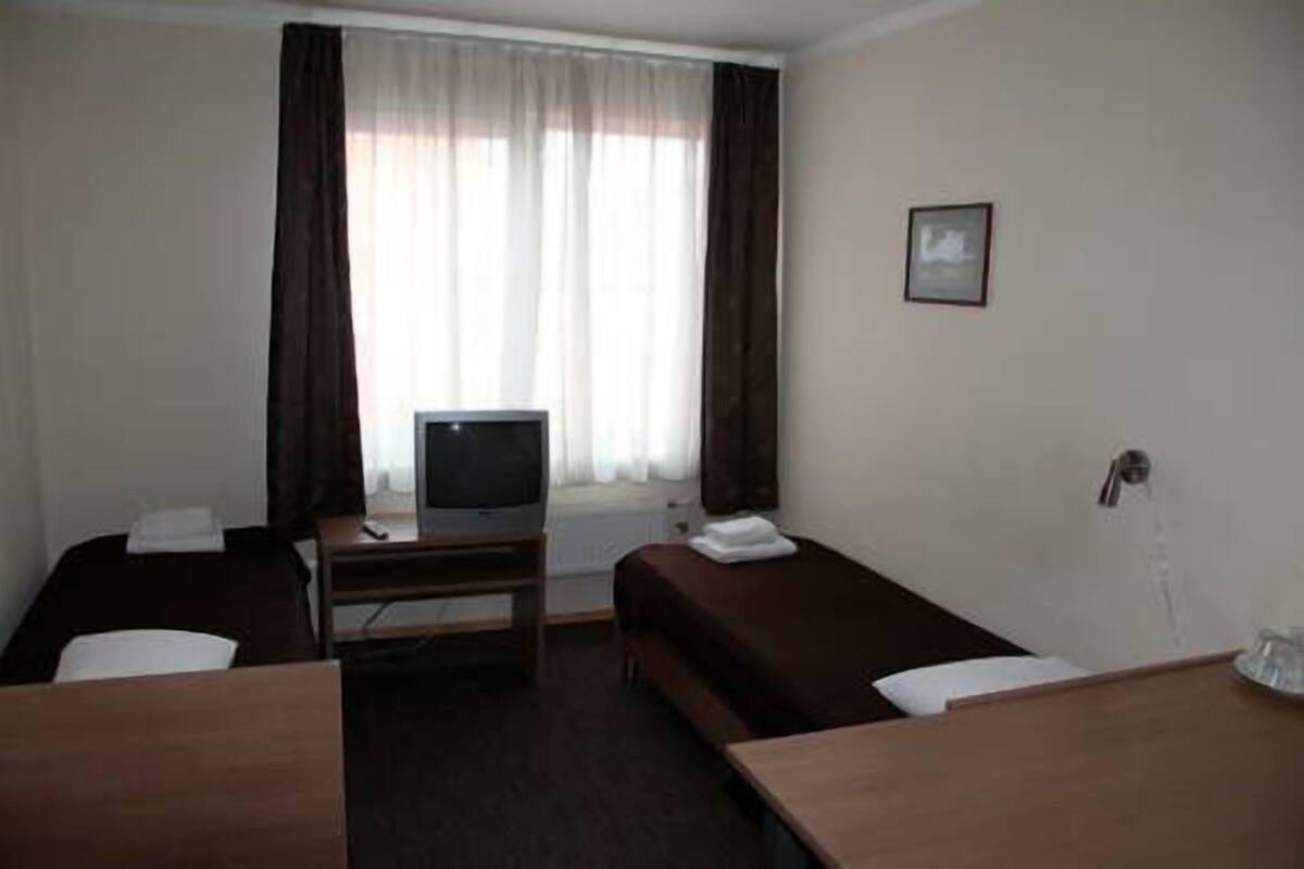 Une chambre d’hôtel avec deux lits simples, un petit bureau avec une télévision et une fenêtre avec des rideaux.