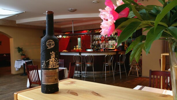 Una botella de vino Khvanchkara sobre una mesa de madera con una barra y sillas al fondo.