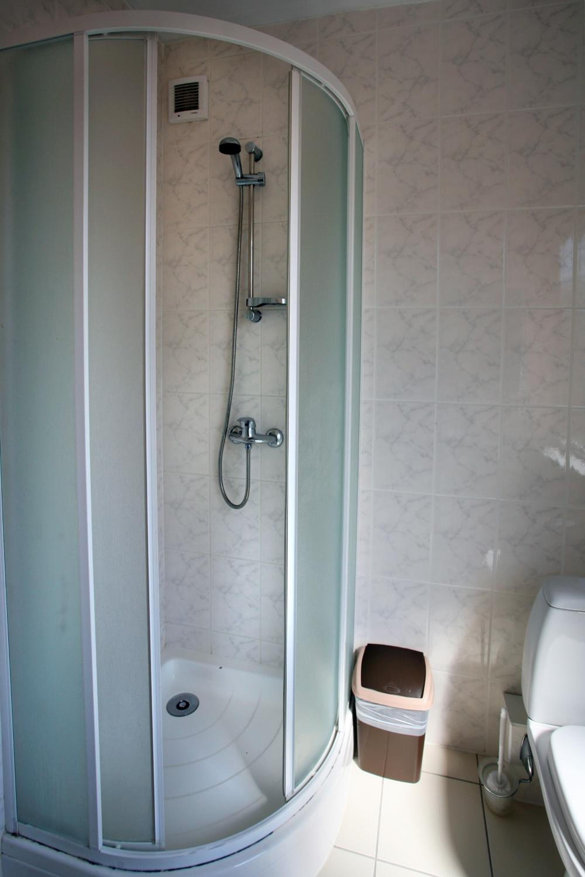 Un baño moderno con cabina de ducha acristalada, inodoro y cubo de basura.