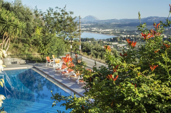 A poolside area with a view of a lake and mountains, surrounded by greenery and outdoor seating. - Alkion (Apokoronas)