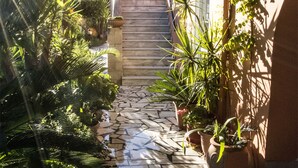 A narrow stone pathway flanked by lush greenery and potted plants, leading up a set of stairs. - Alkion (Apokoronas)