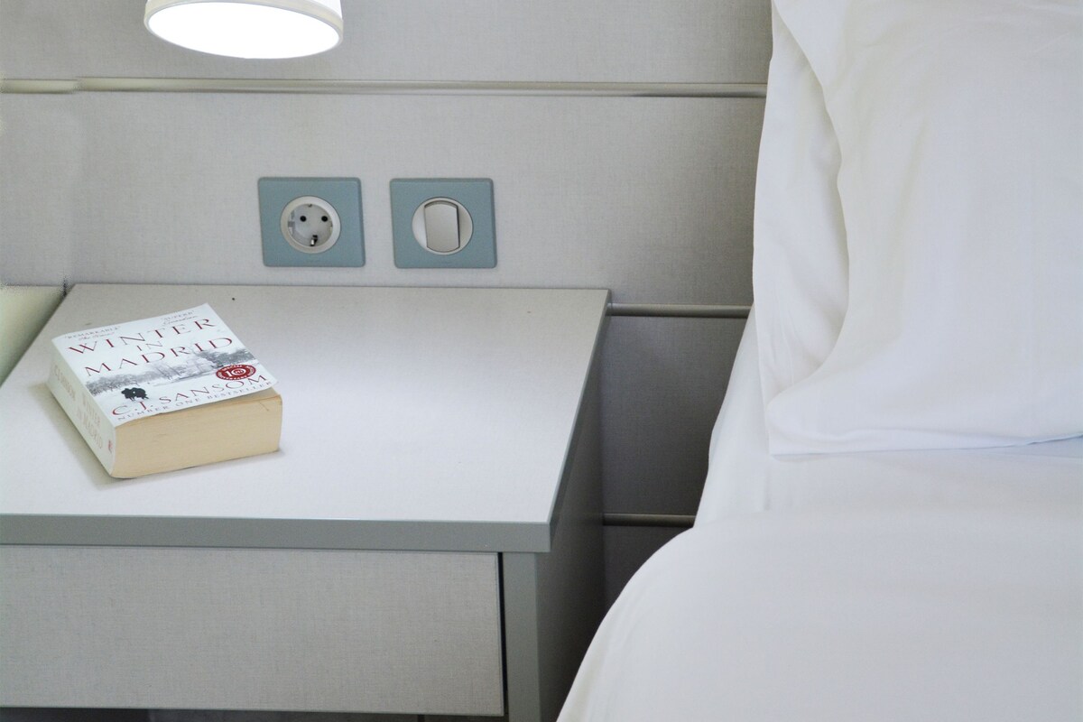 Siisti hotellihuone, jossa on huolitellusti pedattu sänky, yöpöytä lampun kanssa ja kirja.