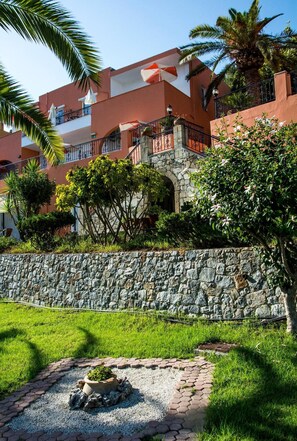 A hotel with a stone wall, lush greenery, and a clear blue sky. - Alkion (Apokoronas)