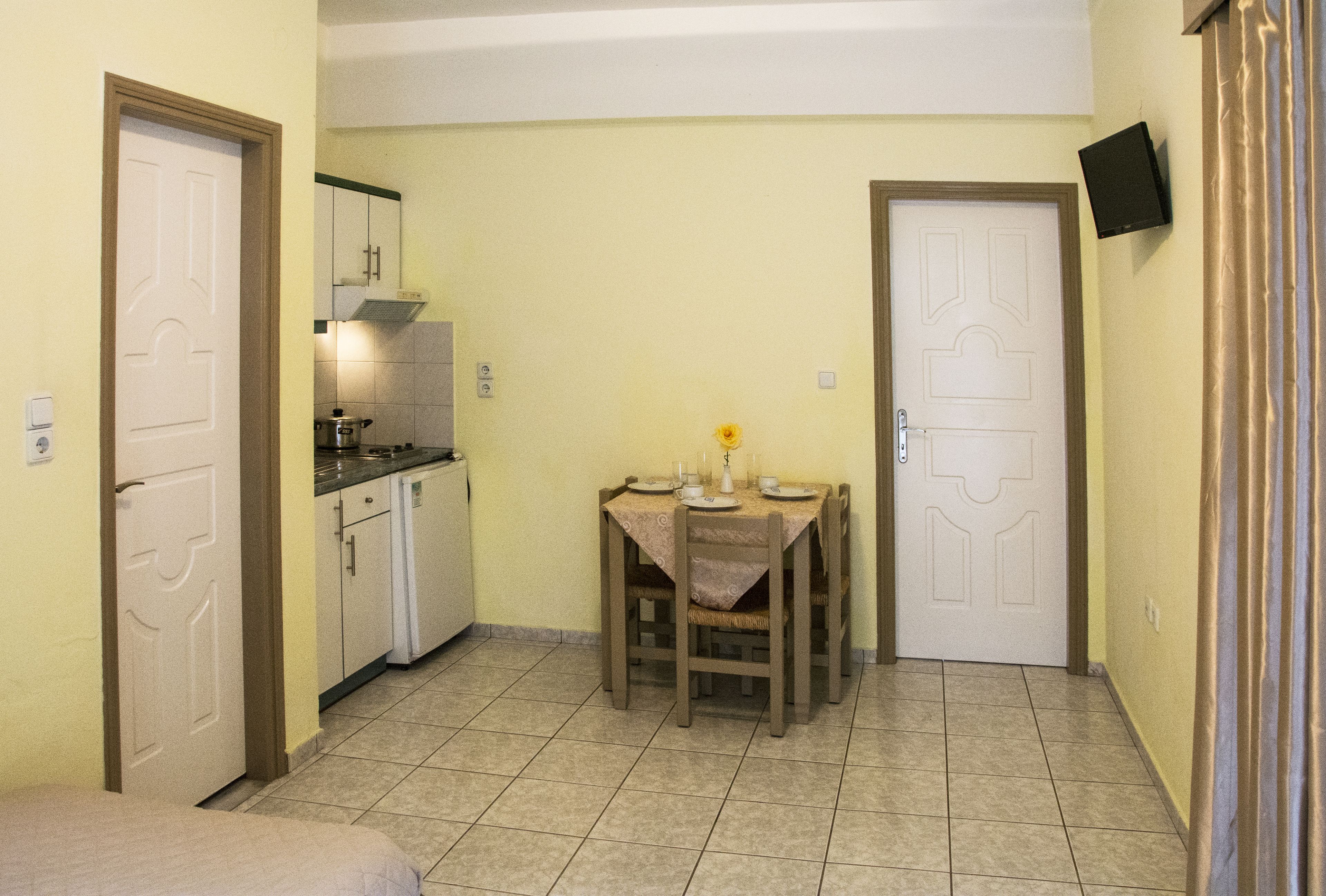 A compact kitchen with a dining area, a small refrigerator, and a TV mounted on the wall.