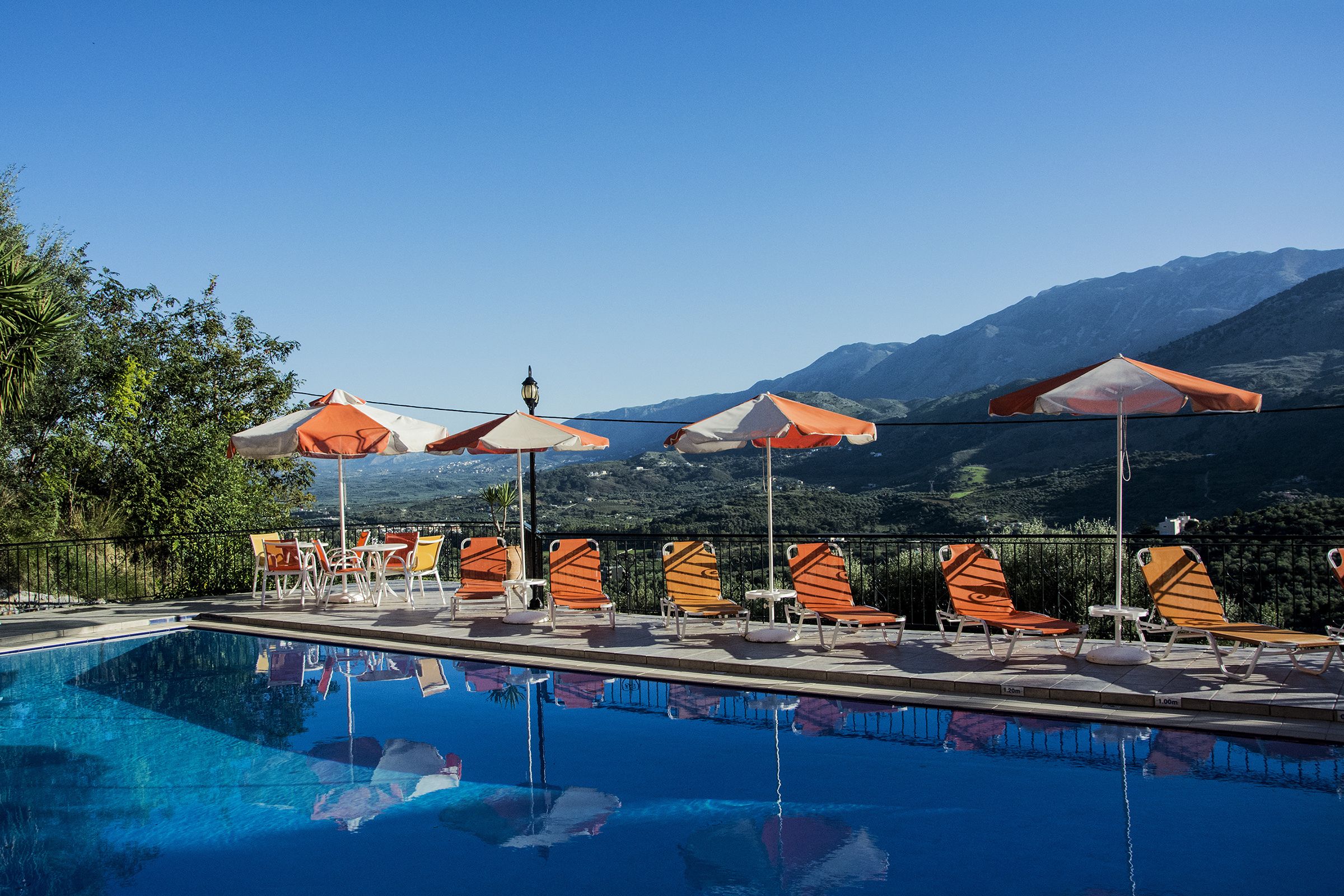 Un área de piscina con sillones de descanso y sombrillas, rodeada de montañas.