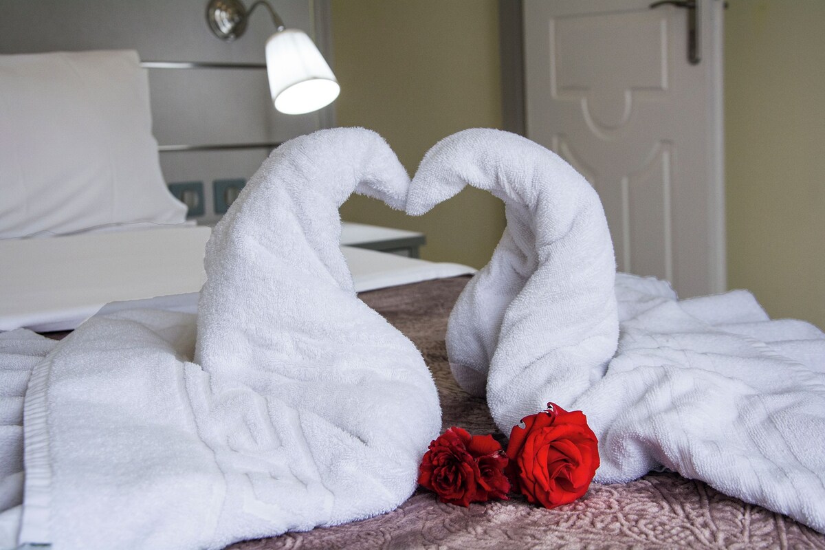 A bed with a white bedspread and two red roses placed on it.