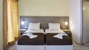 A double room with two beds, each with a pillow and a blanket, a nightstand with a lamp, and a curtain. - Alkion (Apokoronas)