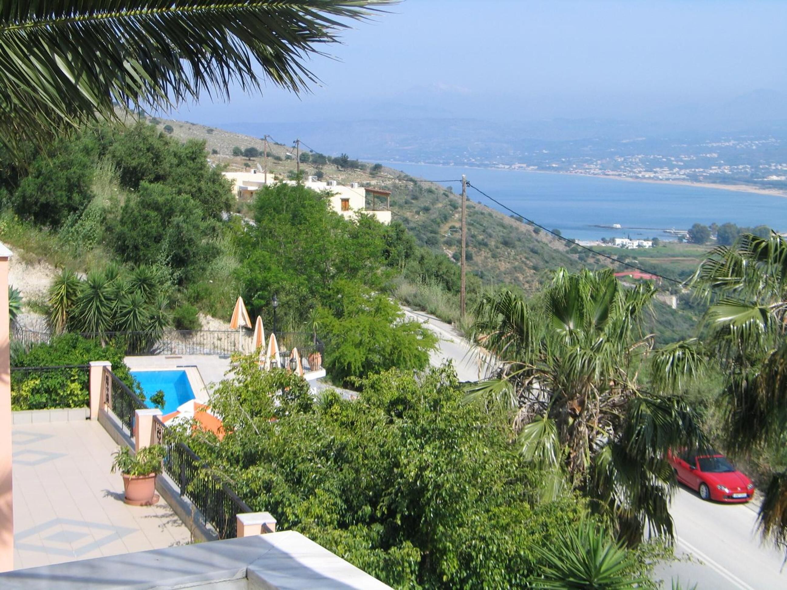 A residential area with a pool, palm trees, and a view of the sea.