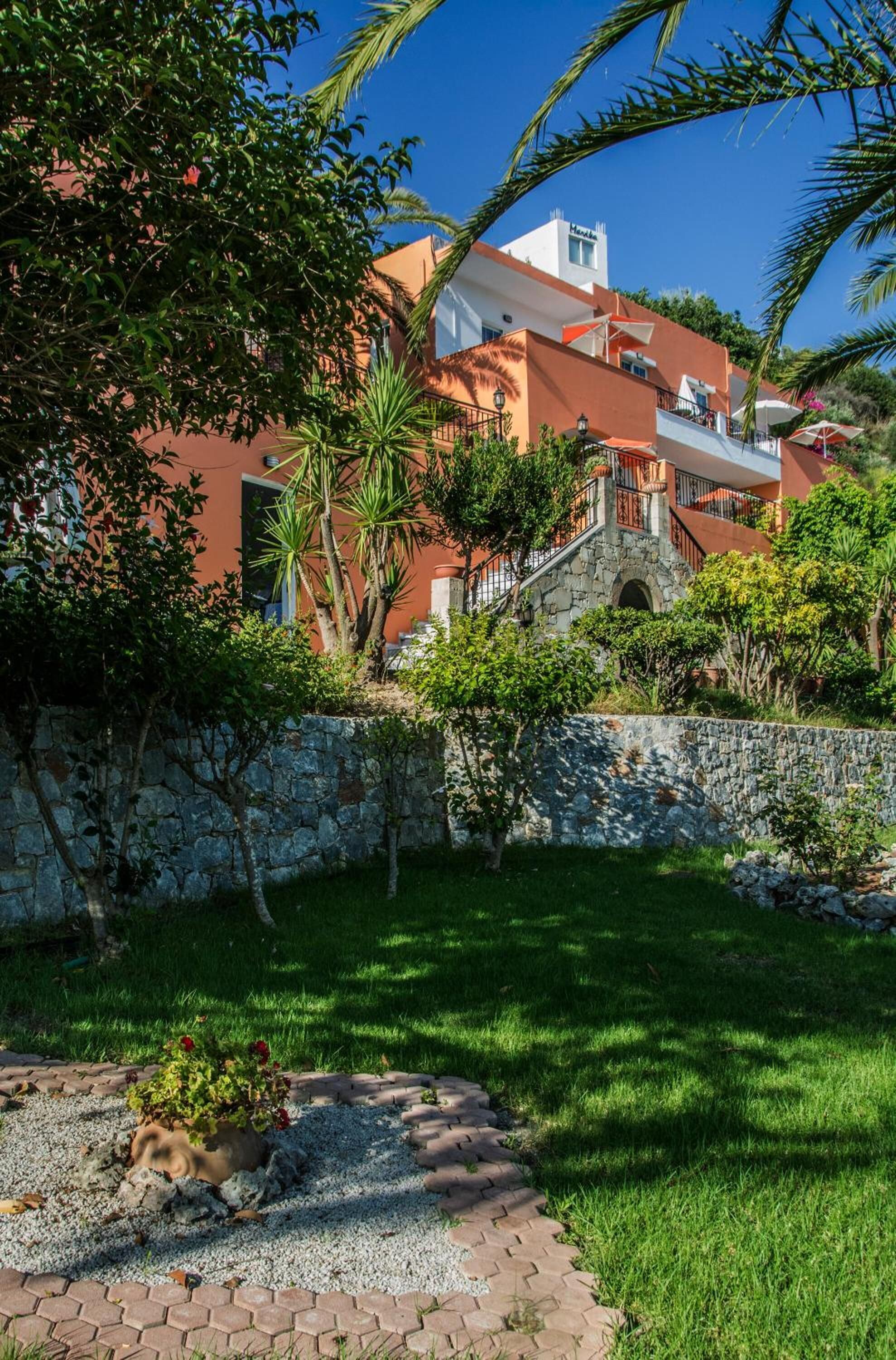 A hotel with a stone wall, a grassy lawn, and a palm tree.