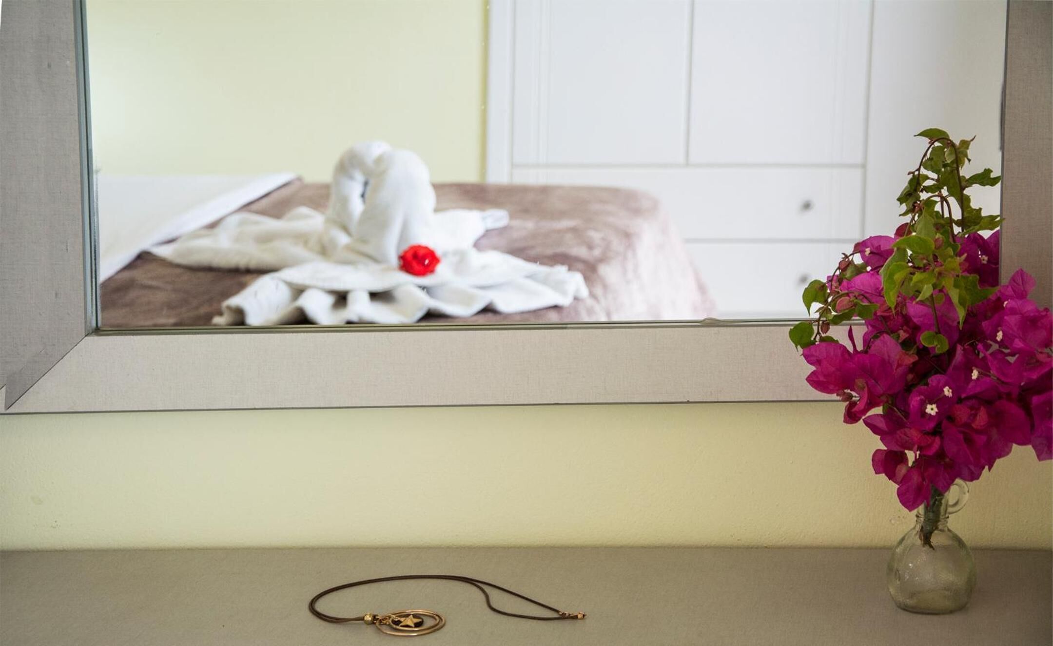 A bathroom with a bed, a towel, a red rose, and a vase with pink flowers.
