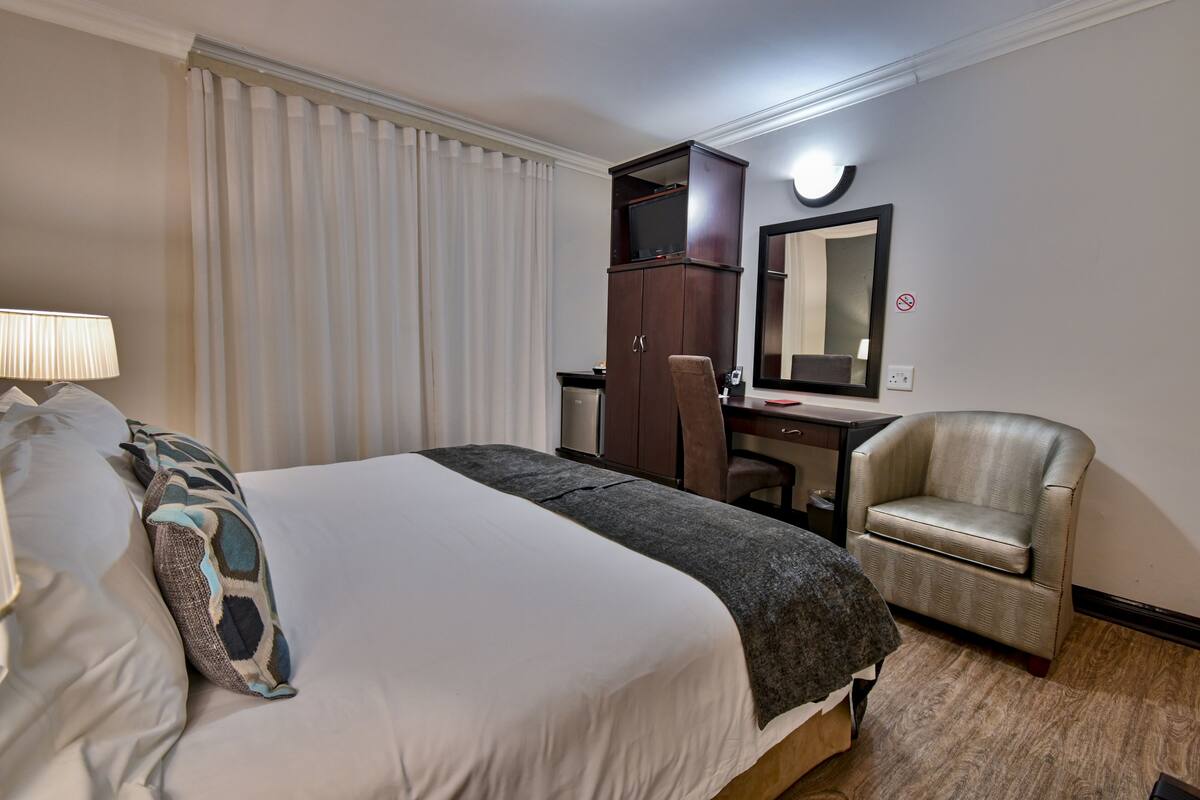 Una habitación de hotel con una cama, un escritorio, una silla, un televisor y un espejo.