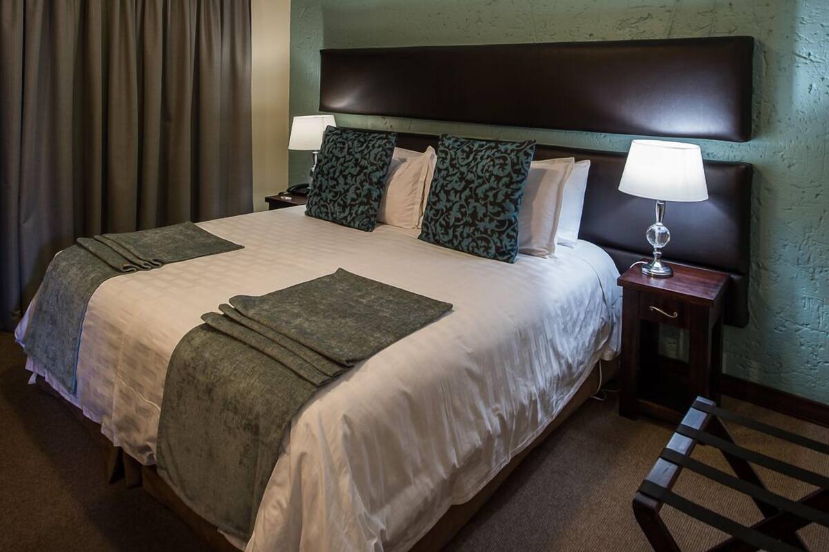 Una habitación de hotel con una cama grande, dos mesitas de noche y un cabecero.
