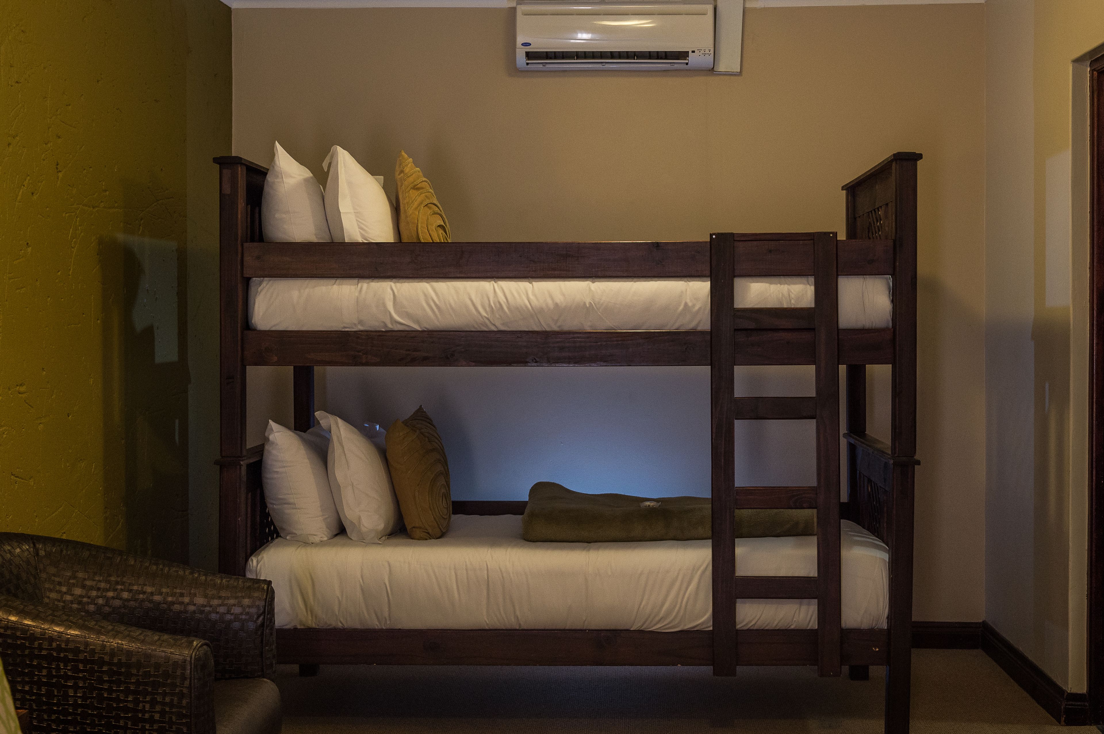 A bunk bed with a ladder, a chair, and an air conditioning unit in a room with plain walls.