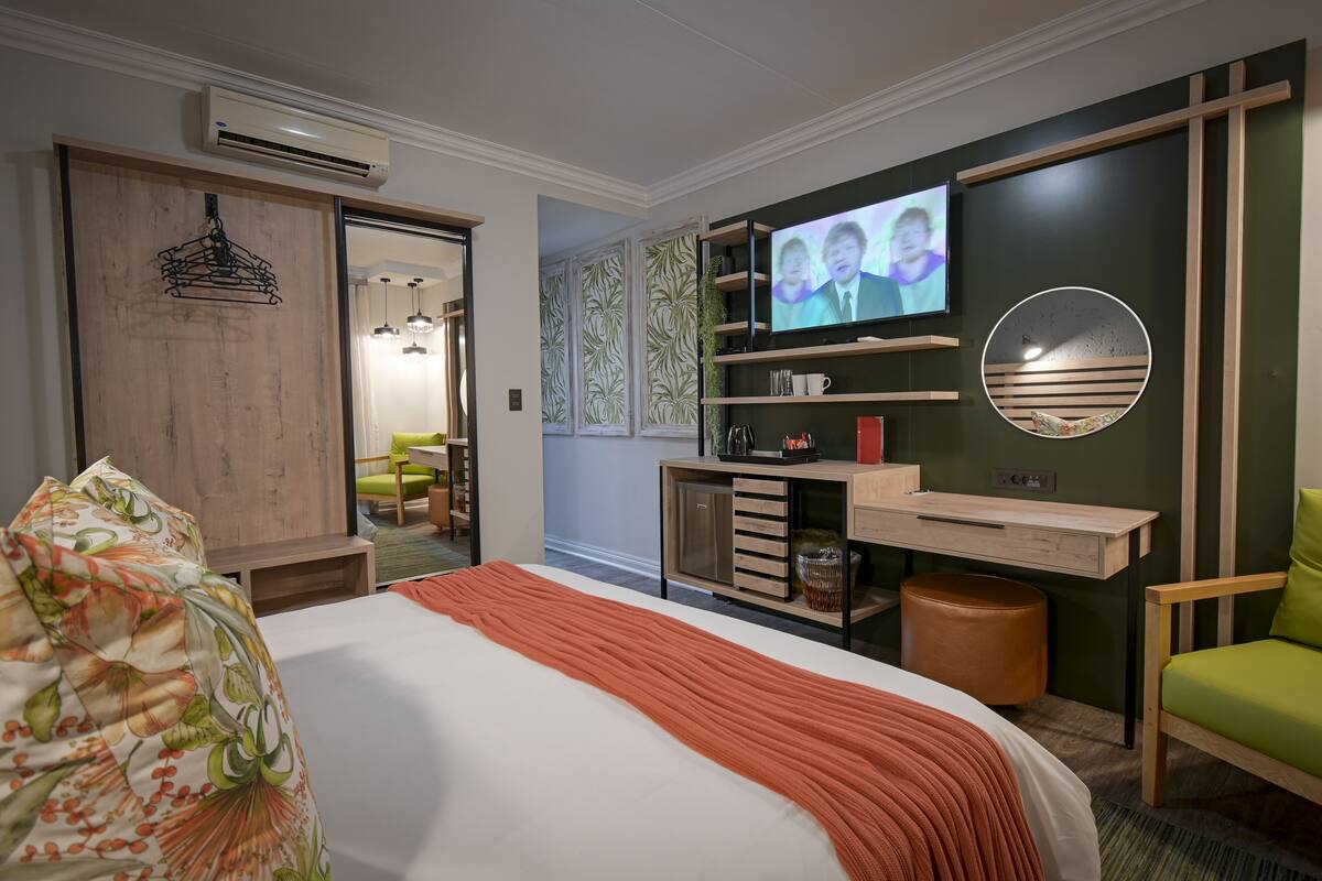 Una habitación de hotel moderna con una cama, un escritorio, un televisor y una silla verde.