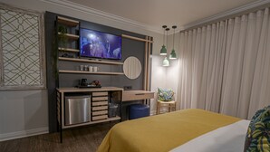 Une chambre d’hôtel moderne équipée d’un lit, d’une télévision, d’un bureau avec un ordinateur, d’une chaise et d’une grande fenêtre avec des rideaux.