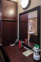 A hotel room with a wooden desk, a mirror, a telephone, and a lamp.