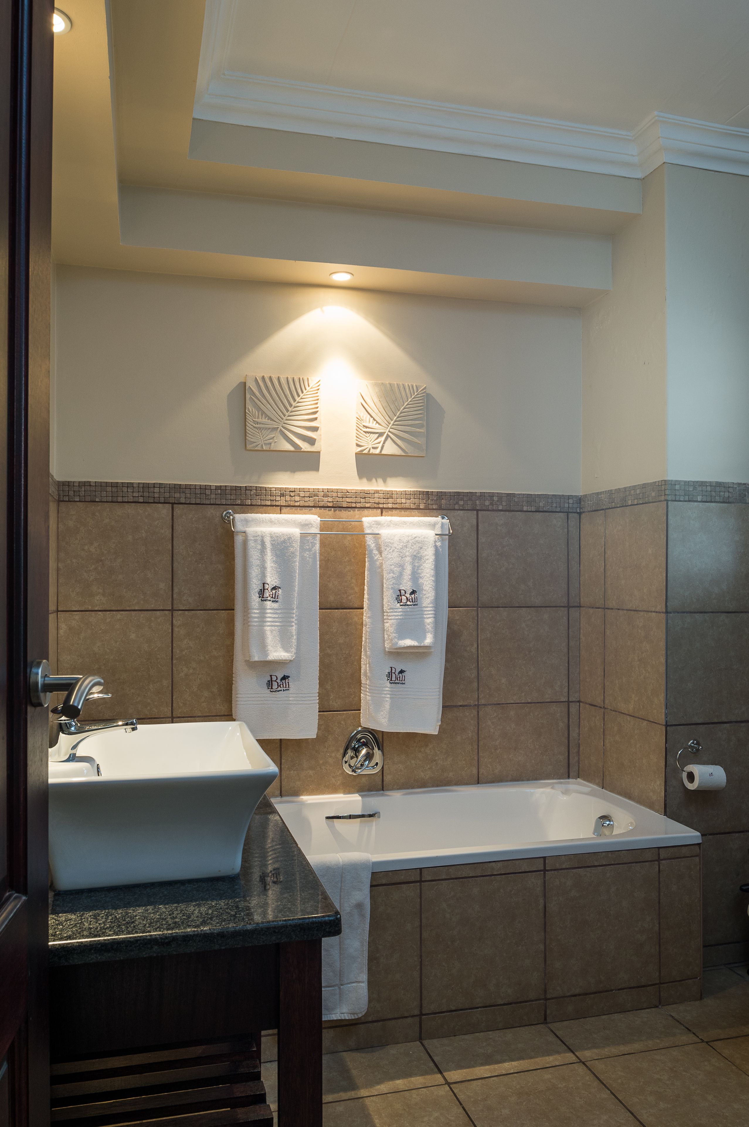 Un baño con lavabo, bañera y dos toallas colgadas en un perchero.