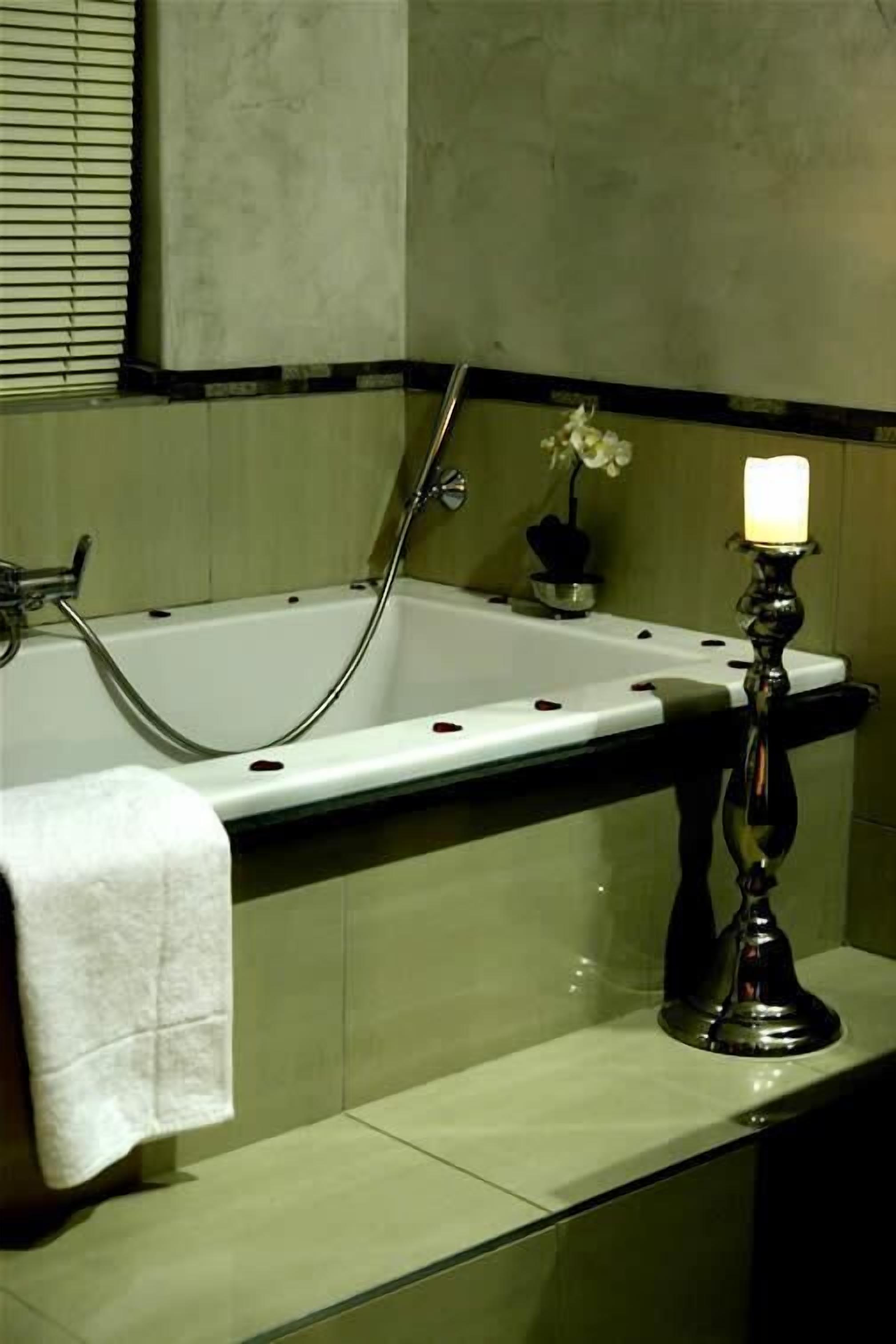 Une baignoire avec une serviette, une bougie et une fleur posées sur le bord.