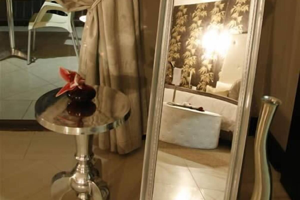 Un grand miroir avec un cadre orné, une petite table sur laquelle est posé un objet décoratif, et un rideau dans une pièce dont le sol est recouvert de carreaux.