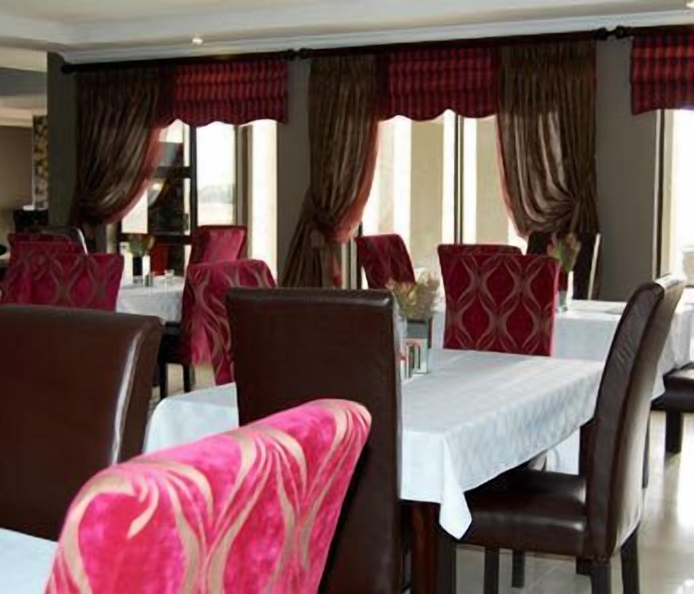Comedor con mesas preparadas para el servicio, cortinas rojas y marrones, y vistas al exterior.