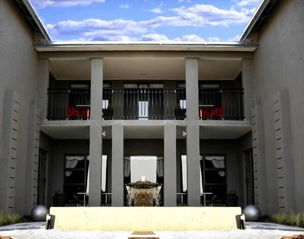 A modern building with a central courtyard, featuring a fountain, two balconies, and a clear sky.