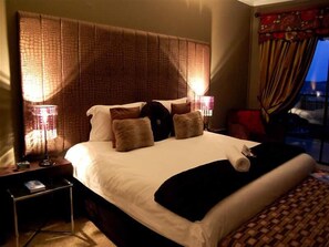 A hotel room with a large bed, two bedside lamps, a nightstand, and a view of the outside.