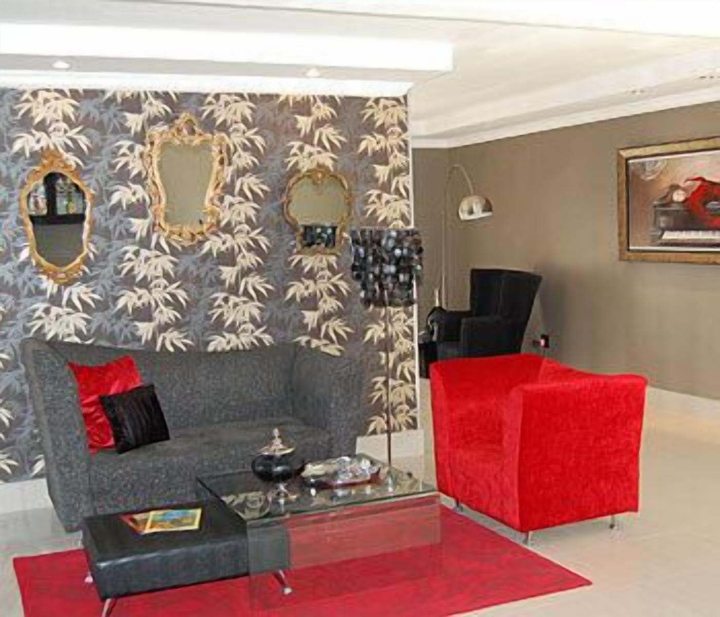 Un salon moderne avec un canapé gris, un fauteuil rouge et une table basse en verre. On y trouve également des miroirs décoratifs et des œuvres d’art murales.