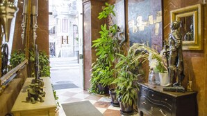 Un hall d’hôtel avec un sol à carreaux, des plantes en pot, une statue et un miroir.