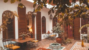 Un patio con suelo de baldosas, una mesa de madera con sillas, un tapete rojo estampado y una planta en maceta.