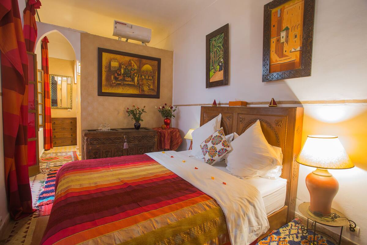 A hotel room with a bed, a nightstand, a lamp, and a painting on the wall.
