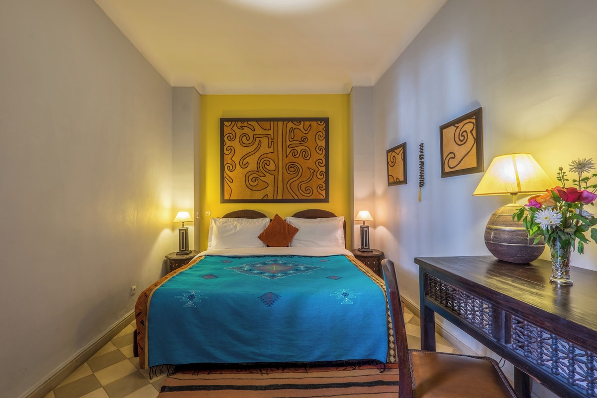 A hotel room with a bed, a nightstand, a lamp, and a decorative wall piece.