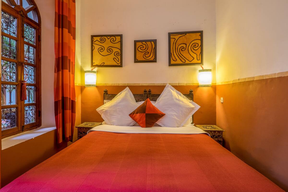 A hotel room with a bed, two wall-mounted lamps, and three framed wall art pieces.