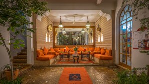 Un rincón acogedor con cojines naranja, una mesa central, plantas en macetas y una alfombra estampada.