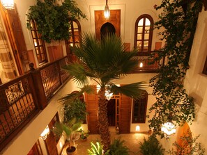 Un atrium à plusieurs niveaux, doté de balcons en bois, d’un palmier central et de plantes suspendues.
