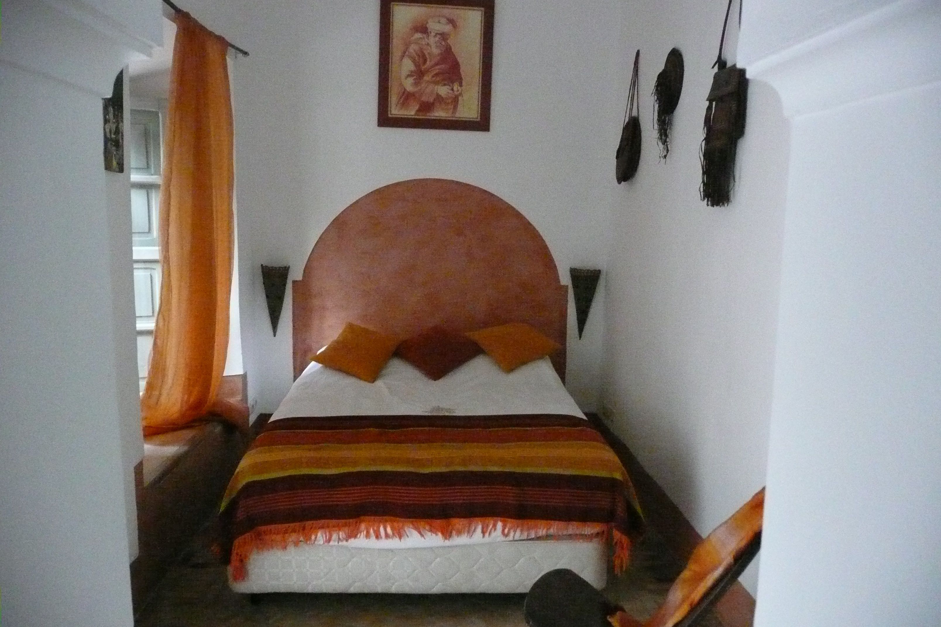 A bedroom with a large bed, a headboard, a wall-mounted picture, and a window with curtains.