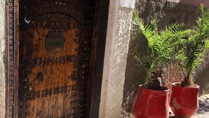 A rustic wooden door with a metal plaque, two red potted plants, and a white wall with a number sign. - Riad Dar Nabila (Marrakech)
