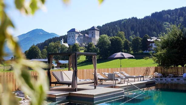 A pool area with lounge chairs, a gazebo, and a view of a castle in the background. - Antonius (Kaprun)