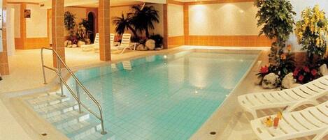 An indoor swimming pool with a tiled floor, a metal ladder, and lounge chairs.