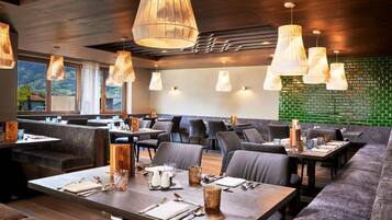 Ein Restaurant mit Holzbalkendecke, grüner Backsteinwand und verschiedenen Sitzbereichen, darunter Tische und Sitzecken.