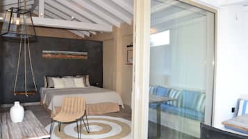 A modern bedroom with a bed, a hanging light fixture, a wicker chair, and a glass door leading to a balcony with a sofa.