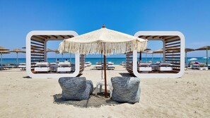 A beach with white lounge chairs and umbrellas, a clear blue sky, and the ocean in the background. - Evilion Sea And Sun (Dio-Olympos)