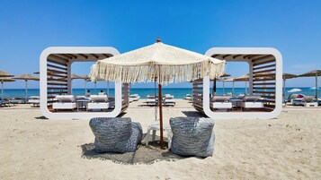 A beach with white lounge chairs and umbrellas, a clear blue sky, and the ocean in the background.