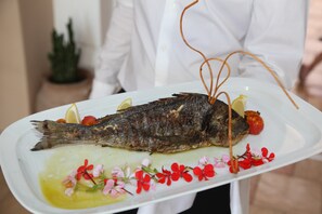 A white plate with a whole fish, lemon slices, and flowers. - Evilion Sea And Sun (Dio-Olympos)