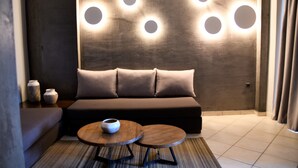 Una sala de estar moderna con un sofá, dos mesas redondas e iluminación circular empotrada en la pared.